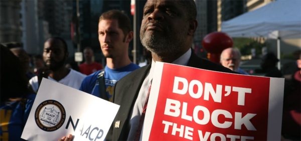 People advocating for their voting rights. A man holds a large sign that says "Don't Block the Vote."