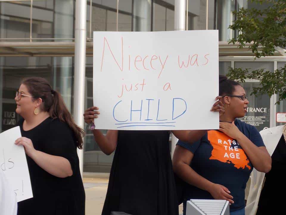 Woman holding a sign that says "Niecey was a child"